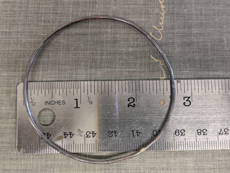 K&ouml;nnte beinhalten: Ein silberner Metallring mit einem Durchmesser von 5 cm, der zur Gr&ouml;&szlig;enbestimmung auf einem Lineal platziert ist.