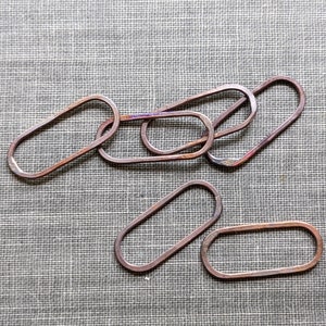 May include: A set of six oval-shaped metal rings, linked together. The rings are a rusty brown color and have a slightly textured surface.