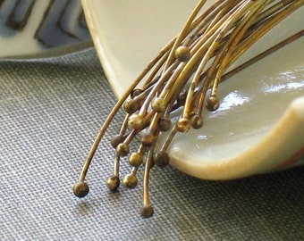 May include: A bunch of gold-colored metal pins with round heads, arranged in a fan shape on a white ceramic surface.