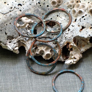 May include: A set of six copper rings with a turquoise patina finish. The rings are stacked on top of each other and are resting on a piece of coral.