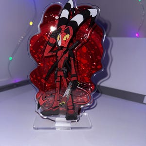 May include: A red and black anime character with horns and a tail, holding a gun, standing on a clear acrylic stand with a red glitter background.