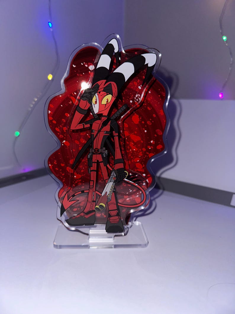 May include: A red and black anime character with horns and a tail, holding a gun, standing on a clear acrylic stand with a red glitter background.