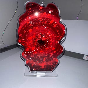 May include: A red and white abstract swirl art piece in a clear acrylic frame with a clear acrylic stand.