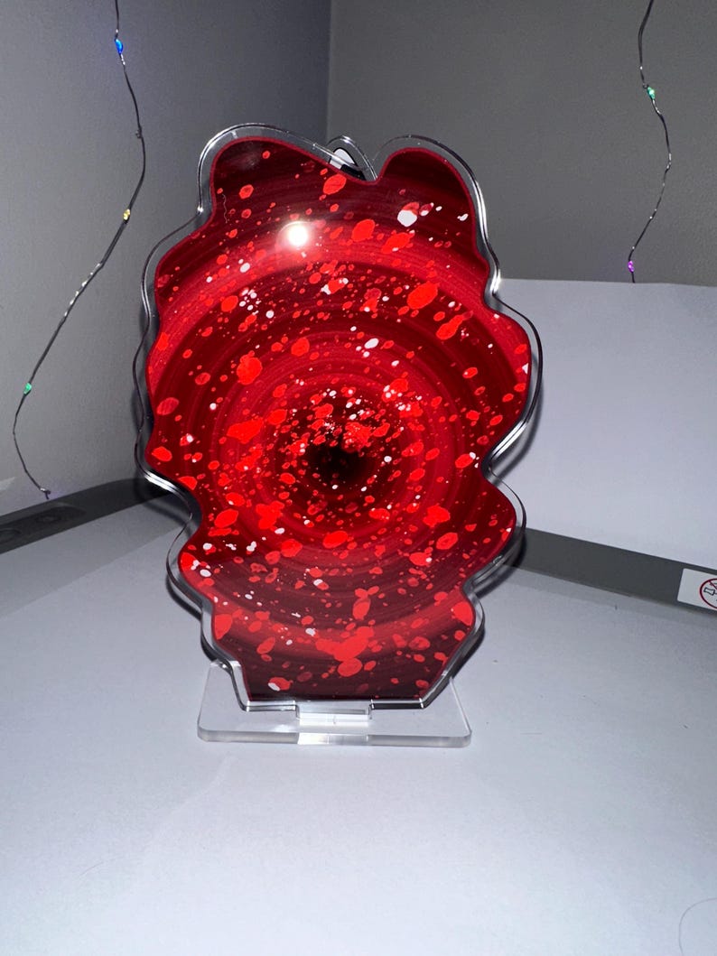 May include: A red and white abstract swirl art piece in a clear acrylic frame with a clear acrylic stand.