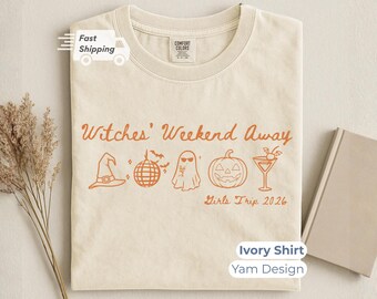 May include: An ivory t-shirt featuring the orange text Witches' Weekend Away and Girls Trip 2026. The graphic includes a witch hat, a disco ball with bats, a ghost wearing sunglasses, a jack-o'-lantern, and a martini glass with a cherry.