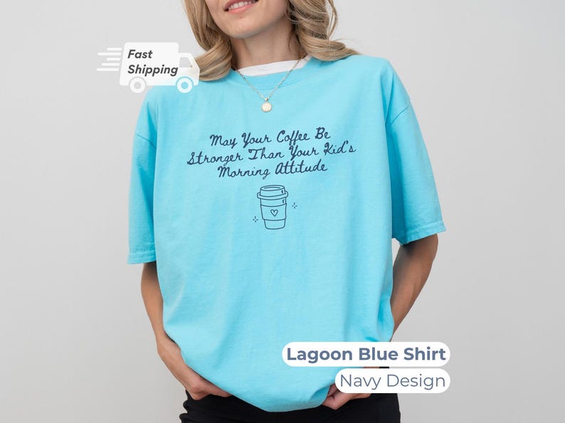 A model wearing a lagoon blue t-shirt with navy blue text reading May Your Coffee Be Stronger Than Your Kid's Morning Attitude and a matching coffee cup graphic.