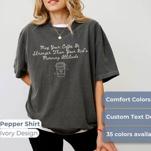 A person wearing a pepper-colored t-shirt with the text May Your Coffee Be Stronger Than Your Kid's Morning Attitude and a coffee cup graphic.