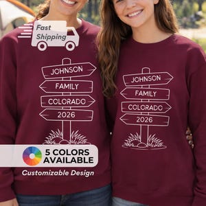 May include: Burgundy sweatshirts with a white signpost design. The signpost reads "JOHNSON FAMILY COLORADO 2026". The text "5 COLORS AVAILABLE" and "Customizable Design" are also visible. The image shows two people wearing the sweatshirts.