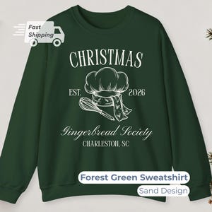 Può includere: Una felpa girocollo verde bosco con una stampa grafica bianca. Il design include un cappello da chef, una frusta e il testo CHRISTMAS, EST. 2026, Gingerbread Society e CHARLESTON, SC. La felpa presenta maniche lunghe e un colletto a coste.