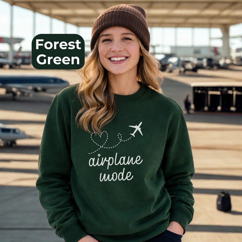 May include: Forest green sweatshirt with the text "airplane mode" and a white airplane graphic. The sweatshirt is a crew neck style and is paired with a brown beanie.