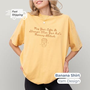 A model posing in a banana yellow t-shirt featuring yam-colored text and a coffee cup outline graphic.