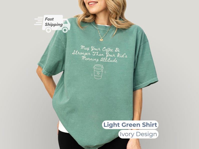 A woman wearing a light green t-shirt with white text that reads May Your Coffee Be Stronger Than Your Kid's Morning Attitude alongside a coffee cup graphic.