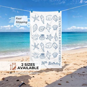May include: White beach towel with a blue seashell pattern and the text "Ocean Tides & Birthday Vibes." The towel is hanging on a clothesline with a beach and ocean background. The text "2 Sizes Available" is also visible.