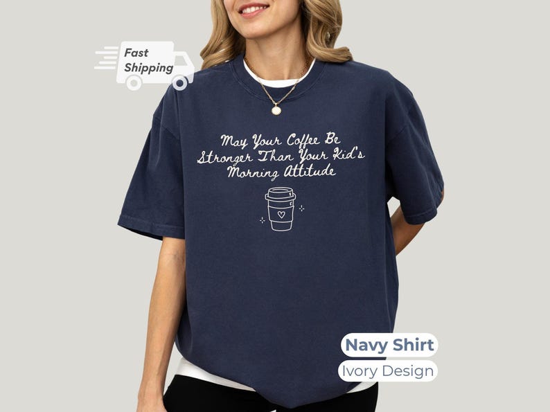 A person wearing a navy blue t-shirt with white lettering that reads May Your Coffee Be Stronger Than Your Kid's Morning Attitude and a coffee cup graphic.