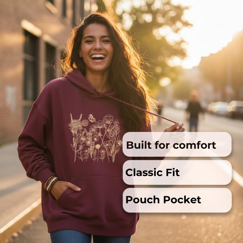 Pu&ograve; includere: Felpa con cappuccio bordeaux con un design floreale dorato. Ha un cappuccio con coulisse e una tasca a marsupio. Il testo sull'immagine dice "Built for comfort", "Classic Fit" e "Pouch Pocket".
