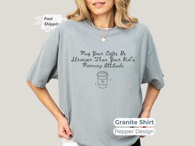 A granite gray t-shirt worn by a smiling model, featuring pepper-colored text and a simple coffee cup graphic.