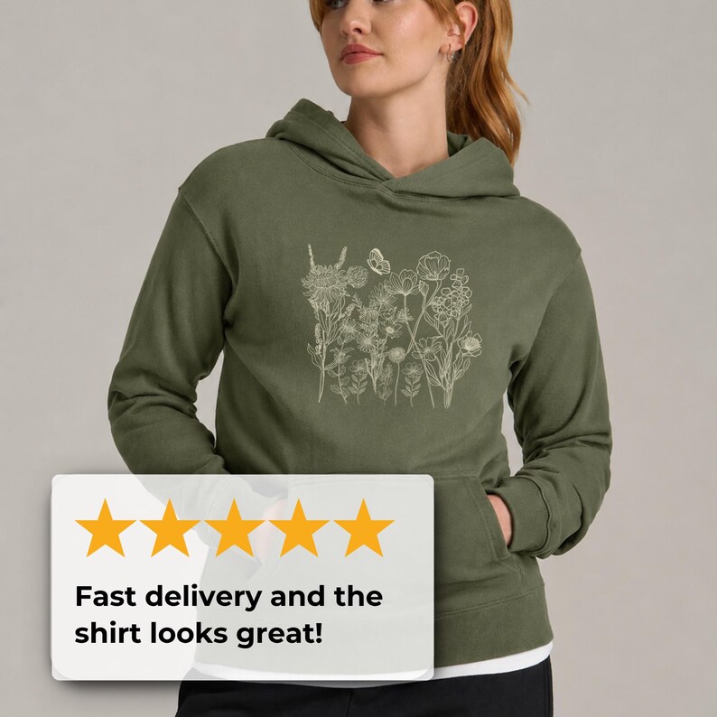 Pu&ograve; includere: Felpa con cappuccio verde oliva con un design floreale bianco e una farfalla. La felpa ha una tasca frontale e un cappuccio. Il testo sull'immagine dice: "Consegna veloce e la maglietta &egrave; fantastica!"