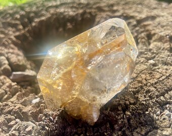 May include: A translucent, multifaceted quartz crystal featuring a clear and golden-yellow coloration with internal fractures and natural inclusions, displaying a sharp, pointed termination and a complex, geometric crystalline structure.