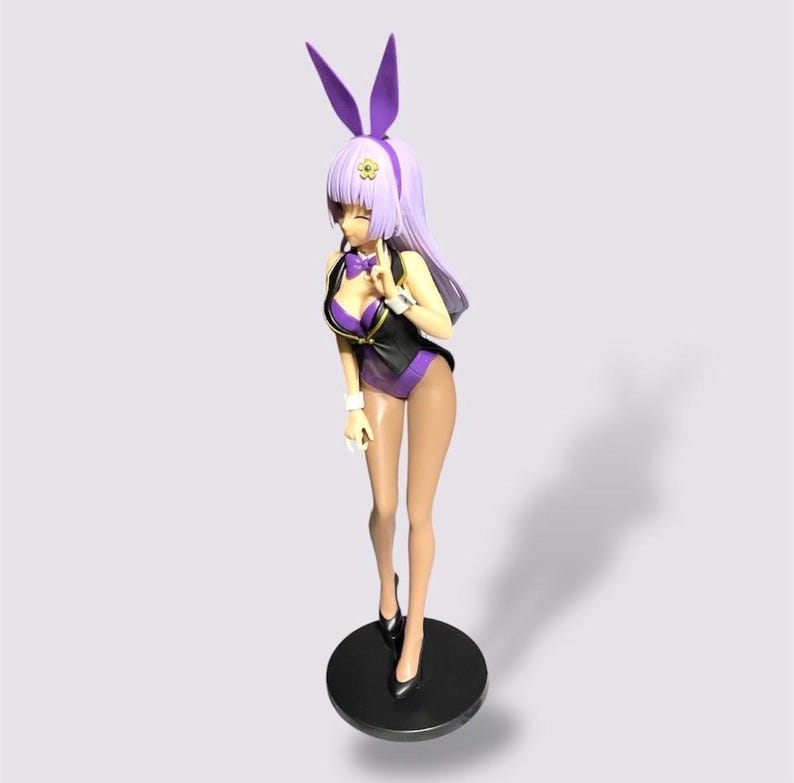May include: A figurine of a woman in a purple and black bunny suit with matching bunny ears. The figure is standing on a black circular base, wearing black heels. The figure has long, light purple hair and is posed with one hand near her face.