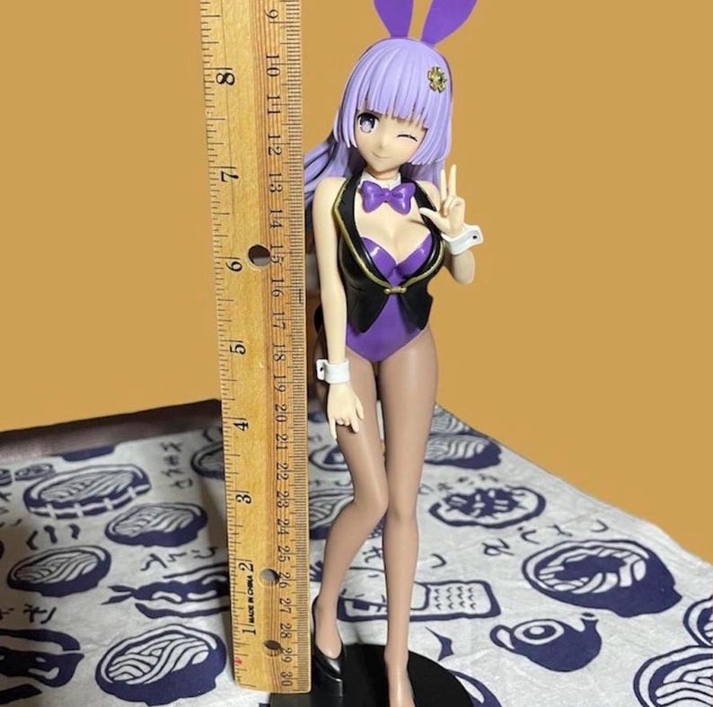 May include: A figurine of a woman in a purple bunny suit with a black vest, purple bow tie, and bunny ears. The figurine is approximately 8 inches tall. The woman is winking and giving a peace sign.