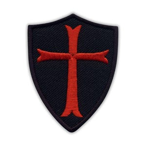 Pode incluir: Um patch preto em forma de escudo com um design de cruz vermelha. A cruz tem extremidades alargadas e está centrada no patch. O patch tem uma borda preta e é provavelmente feito de tecido.