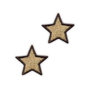 Peut inclure: Deux écussons brodés en forme d'étoile à cinq branches. Chaque étoile présente un centre beige clair avec une bordure cousue marron foncé, mettant en valeur une finition en fil texturé sur l'ensemble de ces deux appliqués en tissu.