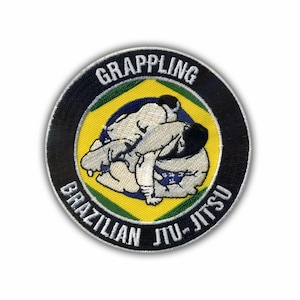 Pode incluir: Um patch circular com as palavras "GRAPPLING" e "BRAZILIAN JIU-JITSU" em letras brancas. Apresenta duas figuras em posição de grappling sobre um fundo amarelo e azul. A borda é preta com uma borda costurada branca.