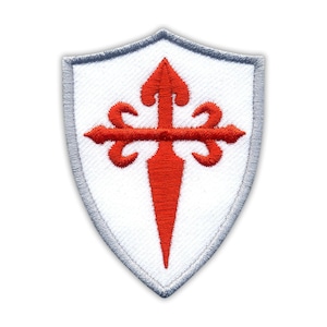 May include: A white shield with a red cross and a pointed tip. The cross has four fleur-de-lis designs at the ends of the cross.