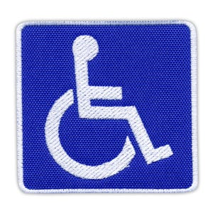 May include: A square, blue patch with a white embroidered wheelchair symbol, indicating accessibility. The symbol is centered on the patch, with a white border. The patch is designed for easy application.