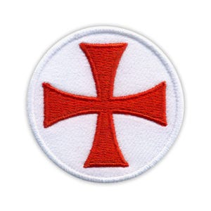 Può includere: Toppa rotonda ricamata con una croce rossa su sfondo bianco. La croce ha quattro bracci di uguale lunghezza, con una forma leggermente svasata. La toppa ha un bordo bianco ed è destinata ai tessuti.