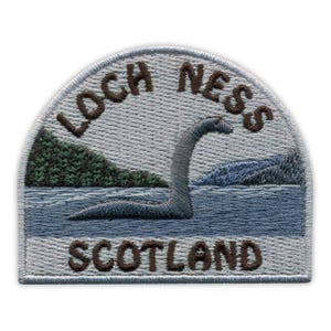 Op de afbeelding: Geborduurde patch met het Loch Ness Monster in een meerlandschap. De patch heeft een lichtblauwe achtergrond met de woorden "LOCH NESS" en "SCOTLAND" in bruin. Het monster is grijs en het water is blauw.