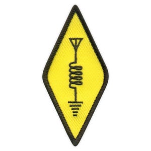 Pode incluir: Um remendo amarelo em forma de diamante com uma antena e uma bobina bordadas em preto.