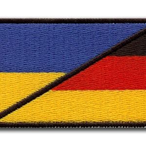 Può includere: Toppa ricamata con un design che combina le bandiere di Ucraina e Germania. La toppa è rettangolare con un bordo nero. La parte superiore sinistra è blu, la parte inferiore sinistra è gialla e la parte superiore destra è rossa, con una linea diagonale nera che separa i colori.