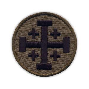 Könnte beinhalten: Ein runder, brauner Patch mit einem dunkelvioletten Kreuz. Das Kreuz ist ein Jerusalemkreuz mit vier kleineren Kreuzen an den Enden der Arme.