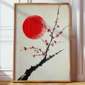 Op de afbeelding: Een ingelijste kunstdruk met een rode zon en een zwarte tak met rode bloesems. Het kunstwerk heeft een minimalistische stijl met een crèmekleurige achtergrond en een houten lijst. De afbeelding roept een gevoel van rust op.