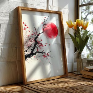 May include: A framed art print featuring a watercolor painting of a red sun and a flowering tree branch. The artwork is in a wooden frame and leans against a white brick wall. A vase of yellow tulips sits on a wooden surface.