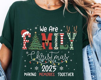 May include: Dark green t-shirt with the text "We Are Family Christmas 2025 Making Memories Together." The design includes a Christmas tree, Santa hat, and reindeer antlers. The shirt is a relaxed fit.