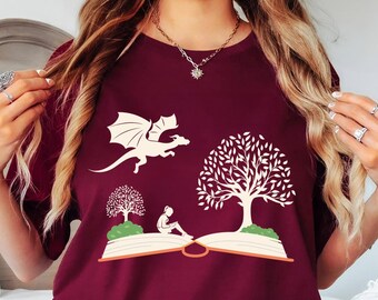 May include: A maroon t-shirt with a white dragon flying out of an open book with a tree on each side. The book has the text "Read" on the spine.