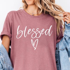 May include: A heather mauve t-shirt with the word "blessed" written in white cursive lettering with a small heart underneath.