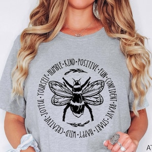 May include: A heather grey t-shirt with a black bee graphic and the text "JOYFUL YOURSELF-HUMBLE-KIND-POSITIVE-FUN-CONFIDENT-BRAVE-SMART-HAPPY-WILD-CREATIVE".