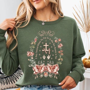 May include: A green sweatshirt with a floral design and the text "O Mary, Conceived Without Sin, Pray for Us Who Have Recourse to Thee" in a circle around a cross and the letters "IM" with a heart.