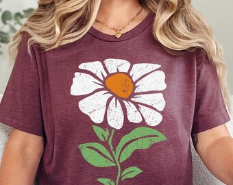 May include: A heather maroon t-shirt with a white daisy graphic. The daisy has a yellow center and green leaves.