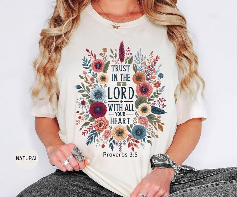 May include: Cream-colored t-shirt featuring a floral design with the text "TRUST IN THE LORD WITH ALL YOUR HEART" and "Proverbs 3:5". The design includes colorful flowers and foliage.