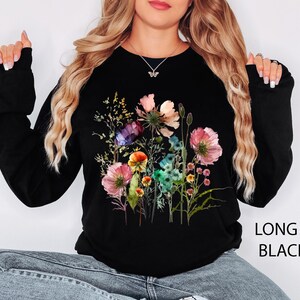 May include: Black long-sleeve sweatshirt featuring a colorful floral design. The graphic includes pink, purple, and yellow flowers with green foliage. The text "LONG S. BLACK" is printed on the lower right side.