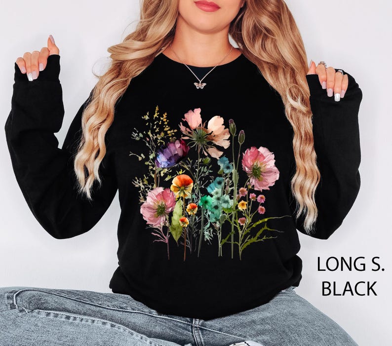 May include: Black long-sleeve sweatshirt featuring a colorful floral design. The graphic includes pink, purple, and yellow flowers with green foliage. The text "LONG S. BLACK" is printed on the lower right side.