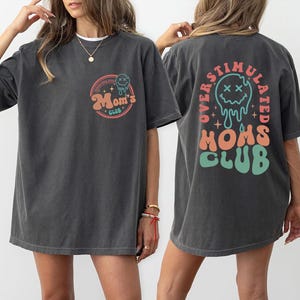 May include: Two charcoal gray t-shirts with the text "Mom's Club" and "Overstimulated Moms Club" in a retro design. The front of the shirt has a circular design with the text "Mom's Club". The back of the shirt has the text "Overstimulated Moms Club".