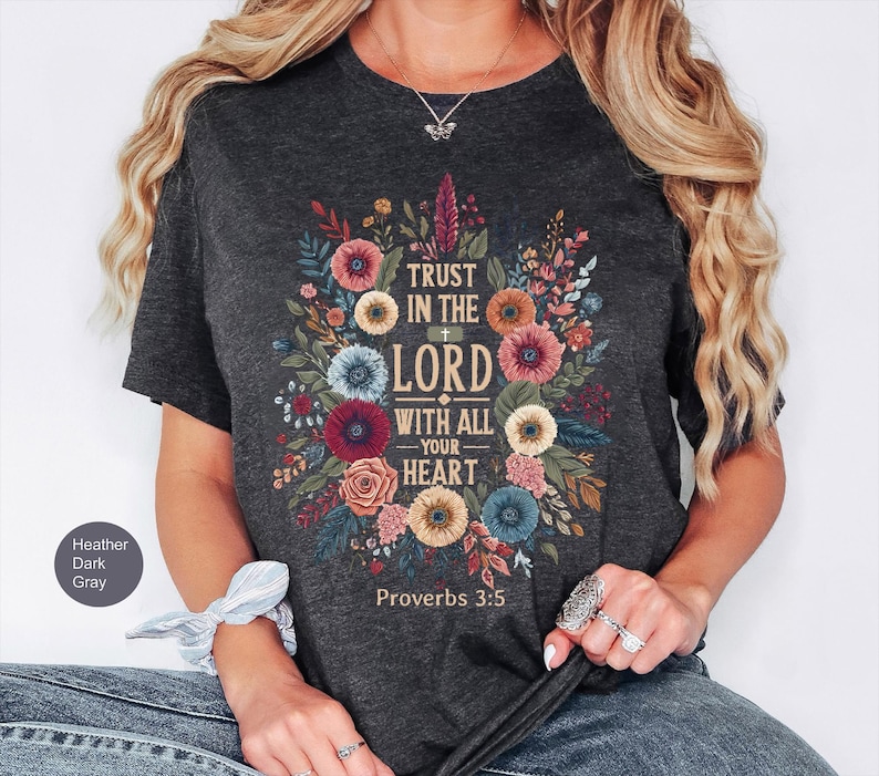 May include: Heather dark gray t-shirt with a floral design and the text "TRUST IN THE LORD WITH ALL YOUR HEART" and "Proverbs 3:5". The design features colorful flowers and leaves.
