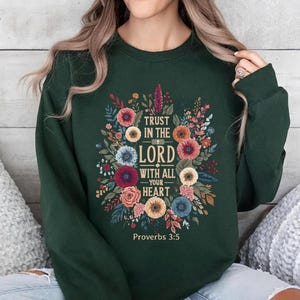 May include: Dark green sweatshirt featuring a floral design with the text "TRUST IN THE LORD WITH ALL YOUR HEART" and "Proverbs 3:5". The design includes colorful flowers and foliage in shades of red, orange, blue, and yellow.