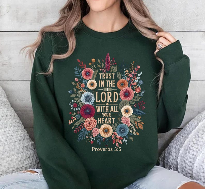 May include: Dark green sweatshirt featuring a floral design with the text "TRUST IN THE LORD WITH ALL YOUR HEART" and "Proverbs 3:5". The design includes colorful flowers and foliage in shades of red, orange, blue, and yellow.