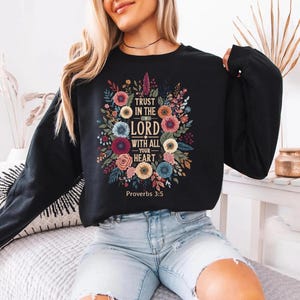 May include: Black sweatshirt with a floral design and the text "Trust in the Lord with all your heart" from Proverbs 3:5. The floral arrangement includes pink, blue, and yellow flowers.